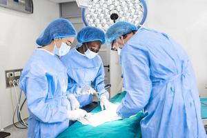 portret van team van multi-etnisch chirurgen Bij werk in een operatie theater. meerdere artsen omgeving geduldig Aan operatie tafel gedurende hun werk. team chirurgen Bij werk in in werking kamer. foto