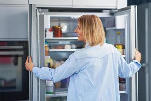 jong volwassen vrouw in de keuken met de koelkast foto