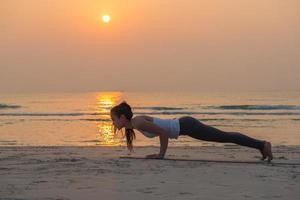 jong Aziatisch vrouw aan het doen yoga oefening Aan de zand strand in de ochtend- Bij zonsopkomst. foto