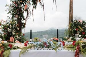 mooi rustiek thema buitenshuis bruiloft wit altaar opstelling, bruiloft zand ceremonie vazen gieten glas bekleed omhoog met natuurlijk bloem decoratie en berg achtergrond. foto