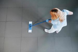 top visie van vrouw in blauw overhemd en beschermend handschoenen dat toepassingen vacuüm schoonmaakster foto