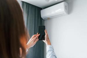 controlerend conditioner door tablet. jong vrouw is binnenshuis in kamer van modern huis Bij dag foto