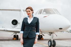 jong stewardess poseren voor de camera buitenshuis in de buurt vliegtuig foto