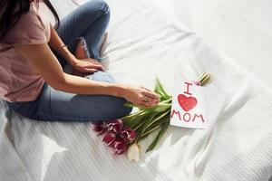 top visie van vrouw dat zit Aan bed met boeket van bloemen en post kaart met hart afbeeldingen Aan het foto