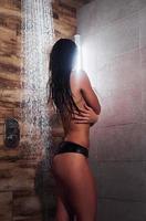 achterzijde visie van brunette met sexy slank lichaam type in ondergoed dat nemen een douche in spa foto