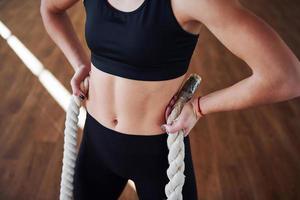 dichtbij omhoog visie van sportief jong vrouw in zwart sportief kleren dat staand met knopen in handen in Sportschool foto