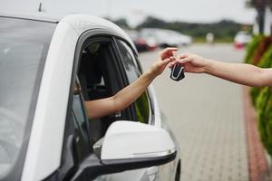 nemen sleutels van de auto. twee mensen. meisje zittend in haar merk nieuw auto- foto