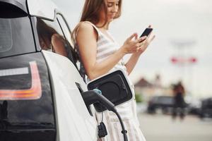 vrouw Aan de elektrisch auto's in rekening brengen station Bij dag. merk nieuw voertuig foto