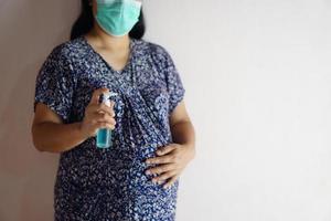 zwanger vrouw houdt fles van hand- ontsmettingsmiddel naar schoon haar handen. concept , Gezondheid zorg gedurende zwangerschap en epidemie van coronavirus of covid-19 en andere kiemen . foto