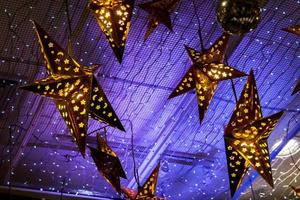 versierd verlichting gouden sterren en blauw lichten van versierd verlichting opgehangen Aan plafond in de kamer voor klaar Aan de Kerstmis nacht feest. foto