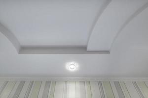 geschorst plafond met halogeen vlekken lampen en gipsplaat bouw met ingewikkeld kroon gieten in leeg kamer in appartement of huis. rekken plafond wit en complex vorm geven aan. foto