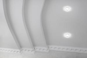 geschorst plafond met halogeen vlekken lampen en gipsplaat bouw met ingewikkeld kroon gieten in leeg kamer in appartement of huis. rekken plafond wit en complex vorm geven aan. foto