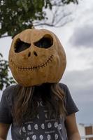 vrouw snijwerk groot oranje pompoen voor halloween terwijl zittend Bij houten tafel Bij huis foto