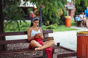 vrouw gebruik makend van een smartphone in park zittend Aan een bank foto