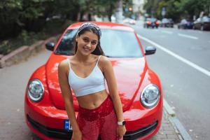 portret van mooi Kaukasisch vrouw staand tegen nieuw rood auto foto