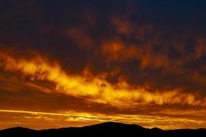 de mooi kleuren van de wolken gedurende zonsopkomst over- heuvels in silhouet foto