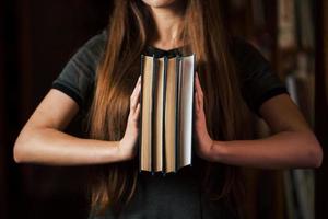 houdt veel boeken in handen. vrouw leerling is in bibliotheek. opvatting van onderwijs foto