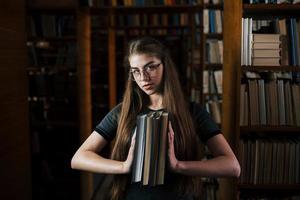 houdt veel boeken in handen. vrouw leerling is in bibliotheek. opvatting van onderwijs foto