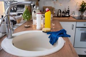 schoonmaak de keuken voordat de Kerstmis en nieuw jaar vakantie. wasmiddel, droog poeder, spons, handschoenen zijn Aan de wasbak. feestelijk decor in de wit keuken, knus interieur van de huis foto