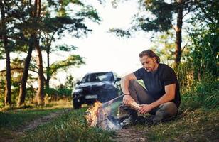 tijd voor een rust uit. Mens in zwart overhemd in de buurt de kampvuur in de Woud Bij zijn weekend tijd foto