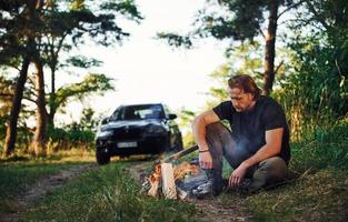 tijd voor een rust uit. Mens in zwart overhemd in de buurt de kampvuur in de Woud Bij zijn weekend tijd foto