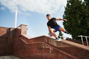 bovenstaand de obstakel. jong sport- Mens aan het doen parkour in de stad Bij zonnig dag foto