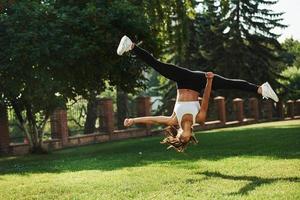gek stunten. jong vrouw aan het doen acrobatisch en parkour trucs in de park foto