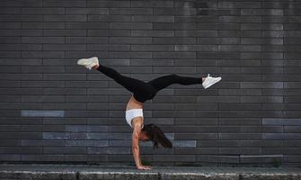 aan het doen gek parkour en atletisch stunten. jong sportief brunette met slank lichaam vorm tegen steen muur in de stad Bij dag foto