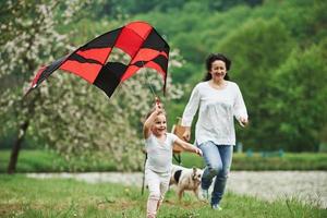 actief spel. positief vrouwelijk kind en grootmoeder rennen met rood en zwart gekleurde vlieger in handen buitenshuis foto