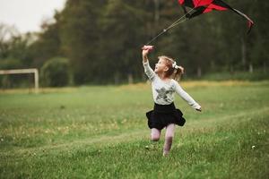 opzoeken. geweldig weer. gelukkig meisje in casual kleding met vlieger in het veld. prachtige natuur foto