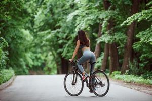 conceptie van snelheid en beweging. vrouwelijke fietser op een fiets op asfaltweg in het bos overdag foto