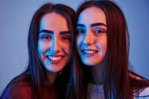 positief zusters. studio schot binnenshuis met neon licht. foto van twee mooi Tweelingen