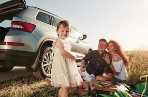 kind in centrum van ieders aandacht. familie hebben picknick Bij platteland in de buurt zilver auto- Bij zonsondergang foto