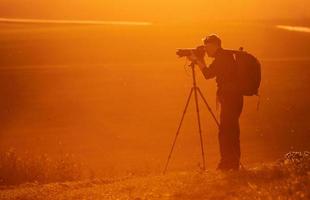 fotograaf met professioneel uitrustingen maakt foto's. staat in de veld- verlichte door zonlicht foto