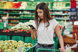 groenten en vruchten. vrouw klant in gewoontjes kleren in markt op zoek voor producten foto