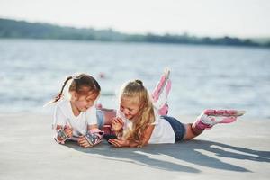 twee weinig meisjes met rol skates buitenshuis in de buurt de meer Bij achtergrond foto