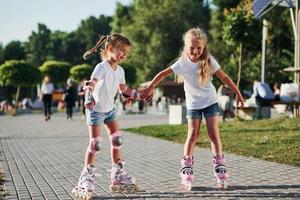 twee schattig kinderen rijden door rol skates in de park Bij dag foto