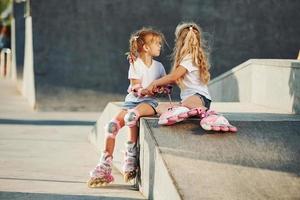 Aan de oprit voor extreem sport. twee weinig meisjes met rol skates buitenshuis hebben pret foto