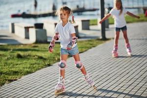 twee schattig kinderen rijden door rol skates in de park Bij dag foto