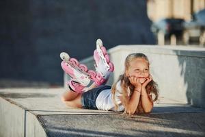 schattig weinig meisje met rol skates buitenshuis zit Aan de oprit voor extreem sport- foto