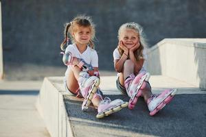 hebben een rust uit. Aan de oprit voor extreem sport. twee weinig meisjes met rol skates buitenshuis hebben pret foto