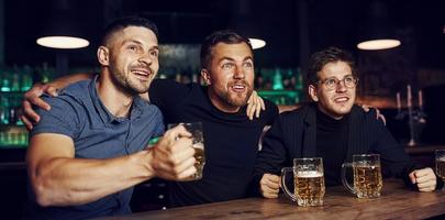 drie sport- fans in een bar aan het kijken voetbal. met bier in handen foto