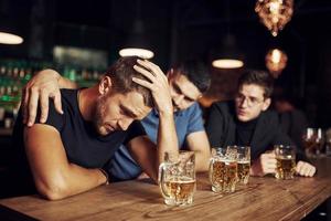 drie mannetje vrienden in de bar. ondersteunen verdrietig vriend. eenheid van mensen. met bier Aan de tafel foto