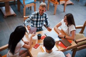 zittend in cafe en hebben gesprek. vier jong studenten in gewoontjes kleren hebben vergadering Bij regenachtig dag foto