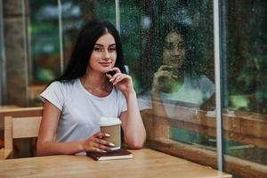 portret van jong vrouw leerling dat zit in cafe Bij regenachtig dag. een persoon enkel en alleen foto