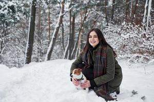 mooi hoor besneeuwd het weer. glimlachen brunette hebben pret terwijl wandelen met haar hond in de winter park foto