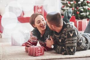 geweldig naar worden samen deze vakantie. lief jong paar aan het liegen Aan de verdieping van leven kamer Bij nieuw jaar tijd met geschenk dozen foto