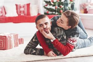 vrouw Toneelstukken met haar echtgenoot. lief jong paar aan het liegen Aan de verdieping van leven kamer Bij nieuw jaar tijd met geschenk dozen foto