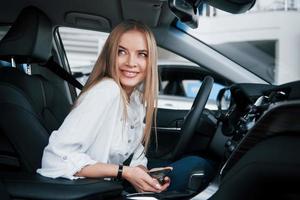 gevoel goed. mooi blond meisje zittend in de nieuw auto met modern zwart interieur foto