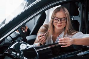 afbeelding in beweging. mooi blond meisje zittend in de nieuw auto met modern zwart interieur foto